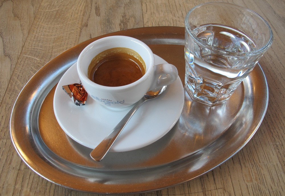 Чашка с кофе на блюдце, чайная ложка, стакан воды на подносе