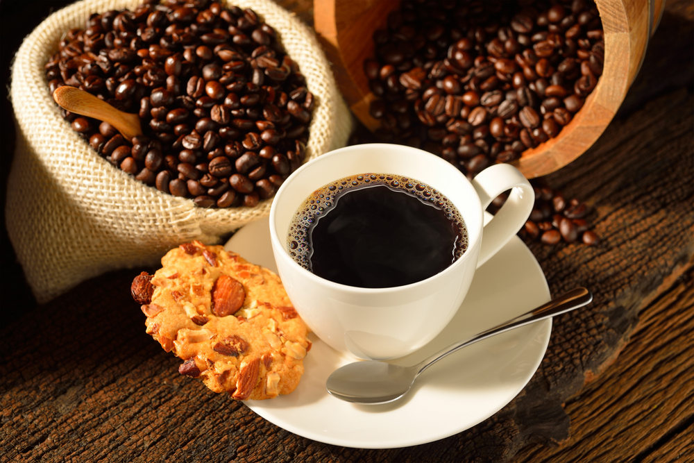 Чашка кофе, чайная ложка, печенье на блюдце, кофейные зерна в мешках