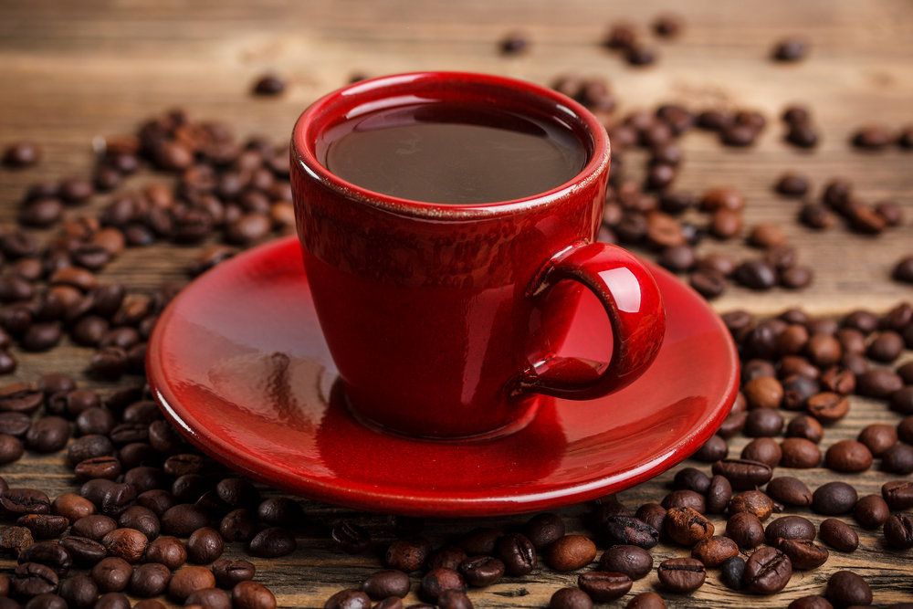 Кофе в красной чашке на блюдце, кофейные зерна на столе